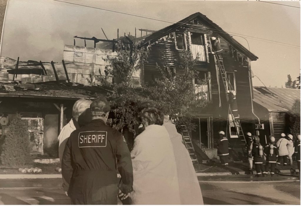 photo of a burned down house and officials standing in front