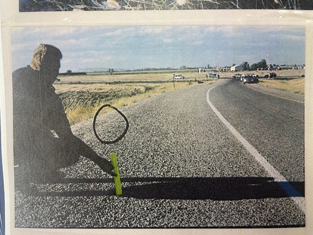 A photo of the crime scene of an officer measuring the distance of possible tire tracks to the shoelaces that were found.