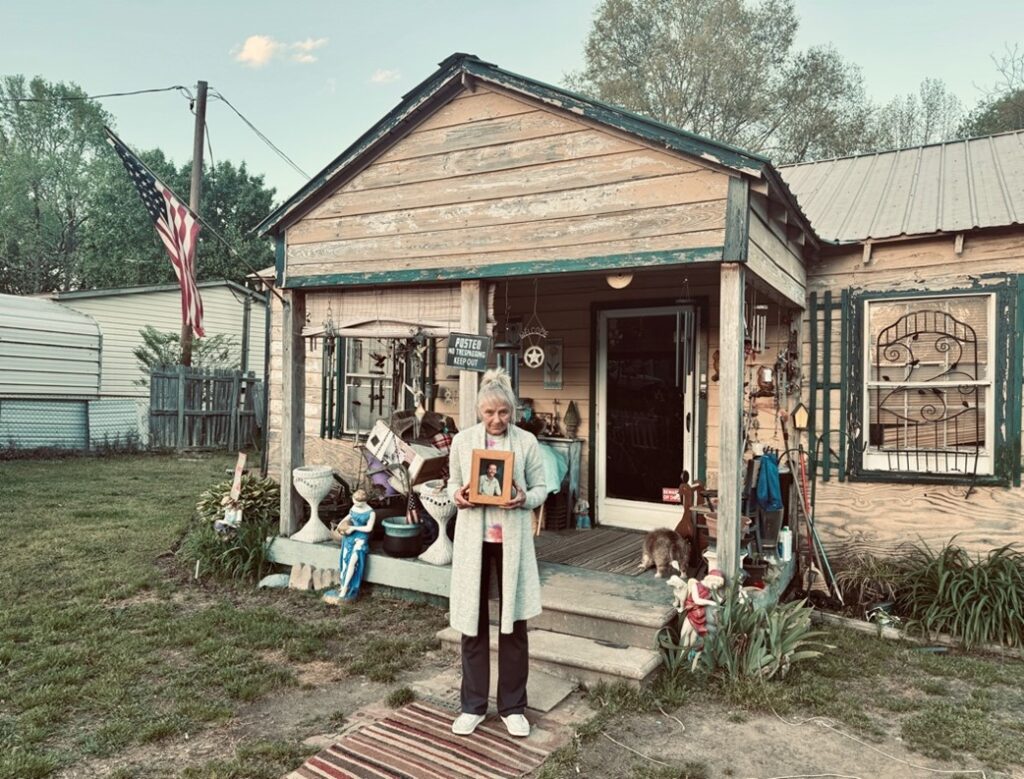 Anita holding Joe’s photo in front of their house.