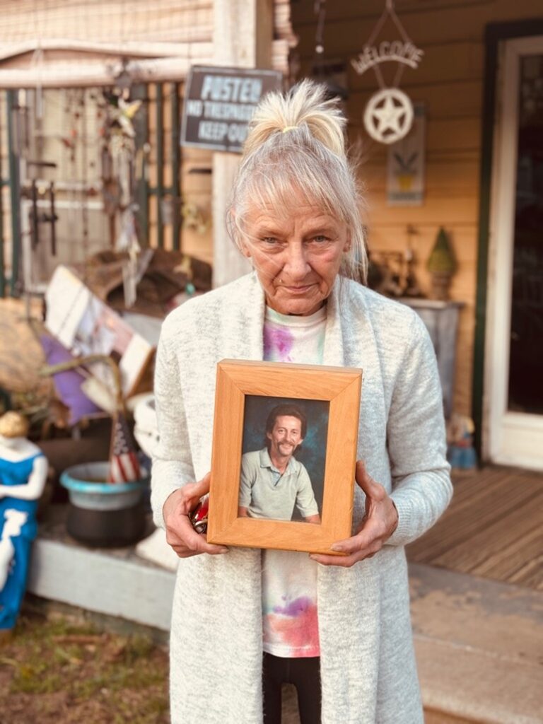 Anita holding Joe’s photo in front of their house.