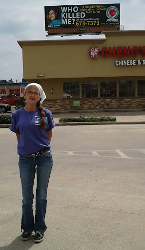 Tammy Meshell stands in the parking lot of a restaurant with a billboard featuring her father’s unsolved murder in the background.